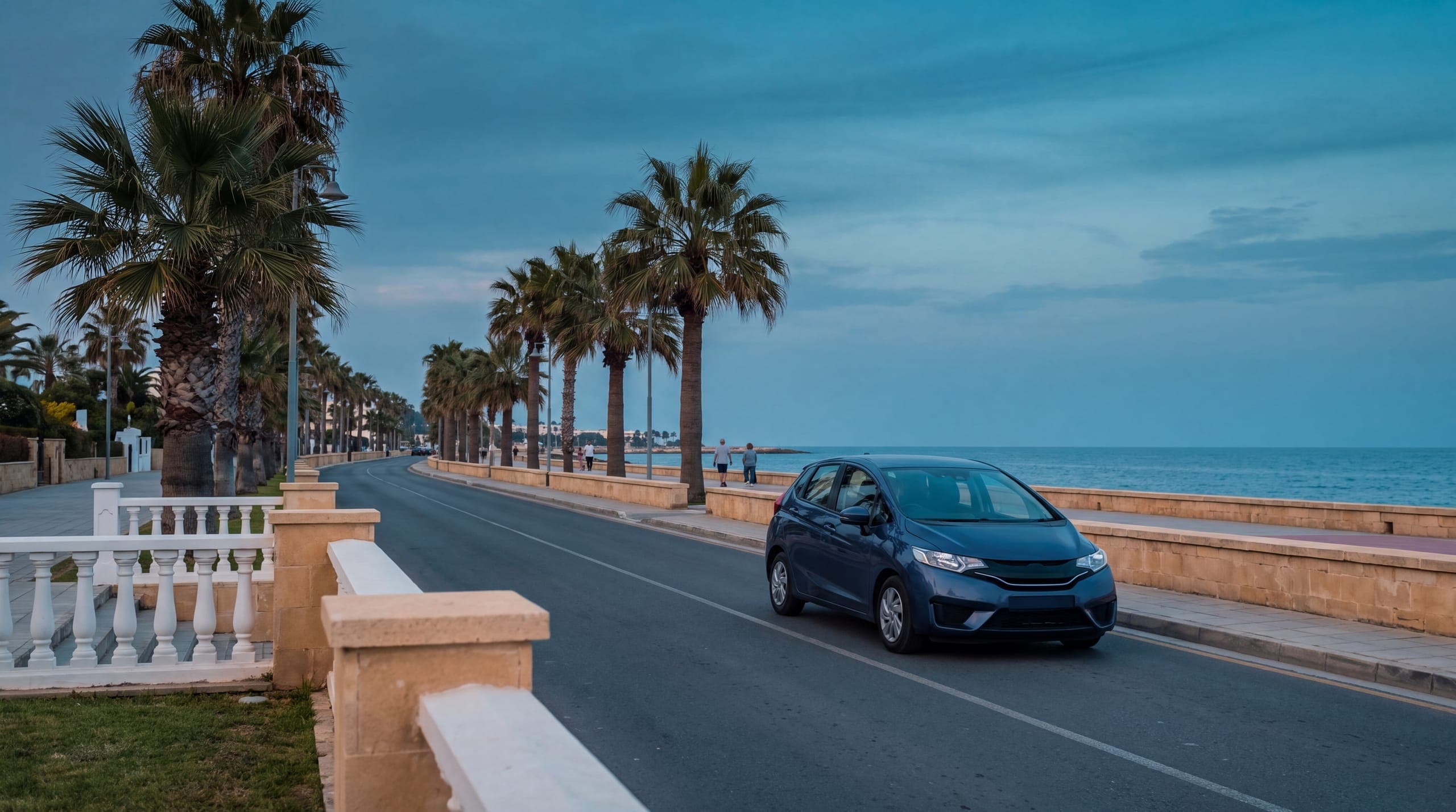 Palm-lined seafront road in Cyprus at dusk, street lamps just lit